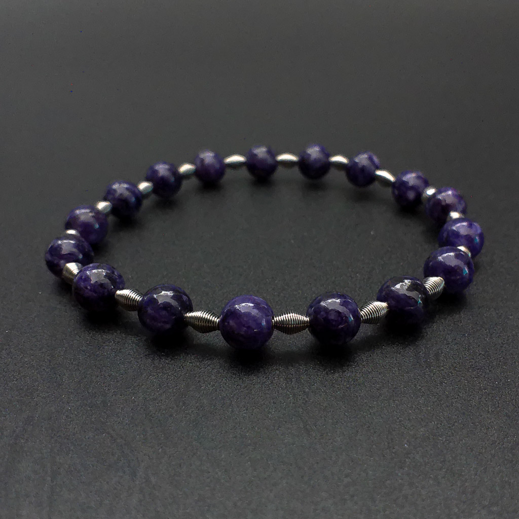 Material: Pulsera elástica con bolas de Charoita y piezas cónicas de acero inoxidable. Diametro pulsera: 6 cm. Tamaño de las Tamaño de las piedras: 6 mm. Propiedades de la piedra: Piedra de transfomación profunda y limpieza. Curación y transmutación de energías. Purifica la mente y aporta sabiduría. Elevación espiritual. Libera miedos y aumenta el campo vibracional. Fomenta la intuición. Reenergiza el plano físico y libera cualquier emoción negativa. Elemento Aire: Espiritualidad, pensamiento, pureza, libertad, renovación. *Las piedras semipreciosas pueden variar ligeramente de tono y forma debido a su origen natural*